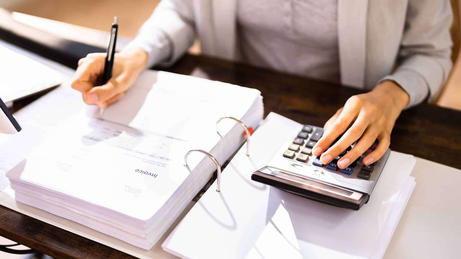 Person calculating taxes with a calculator and reviewing financial documents, emphasizing tax preparation and audit avoidance strategies.