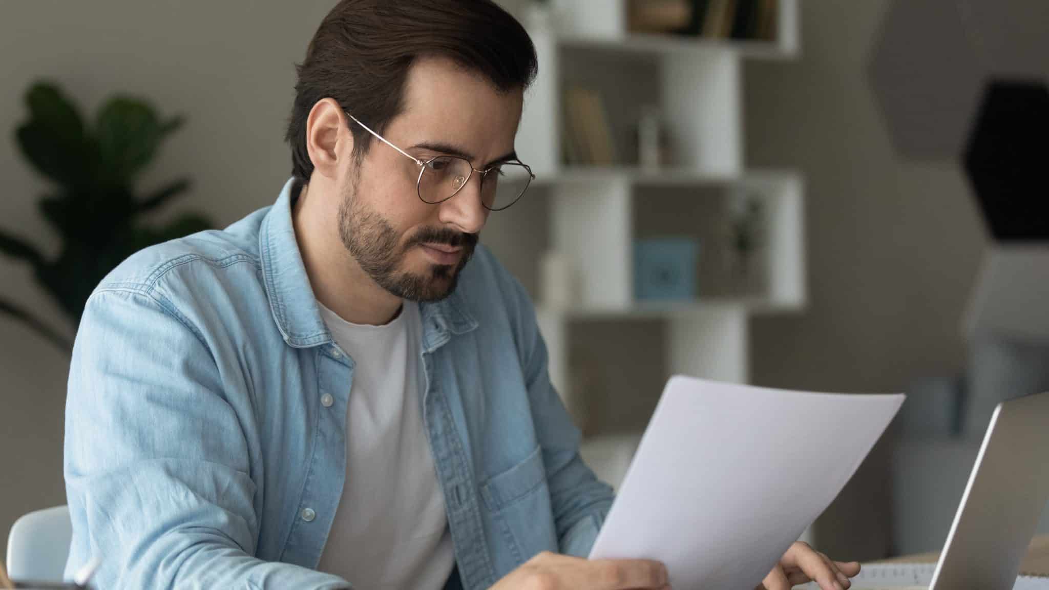 Man reading IRS notice letter at desk, concerned expression, laptop and modern workspace background, emphasizing importance of timely response to tax issues.
